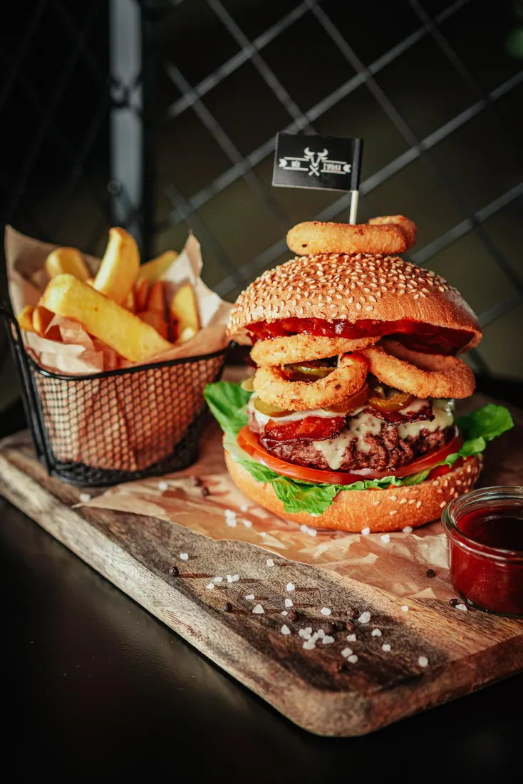 Wysoki burger z krążkami cebulowymi i frytkami